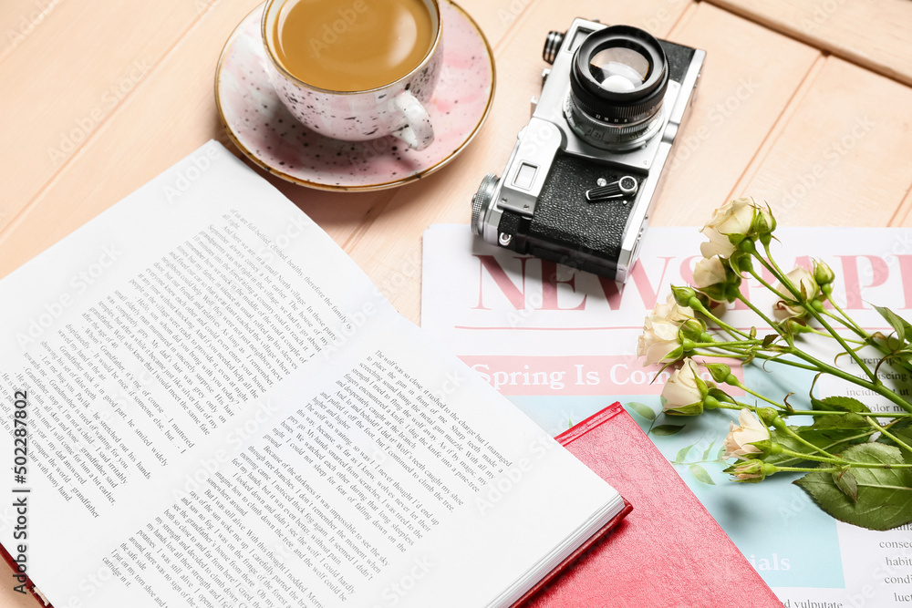 Books, cup of coffee, newspaper, flowers and photo camera on light wooden background