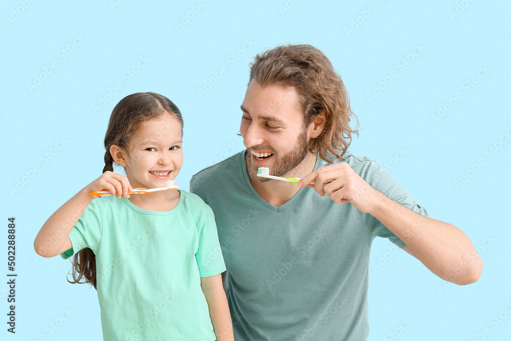 Little girl with her father brushing teeth on blue background