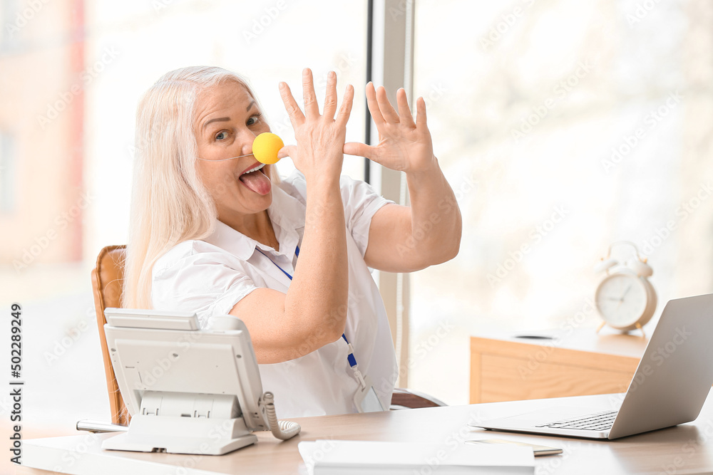 Funny mature woman with clown nose in office. April fools day celebration