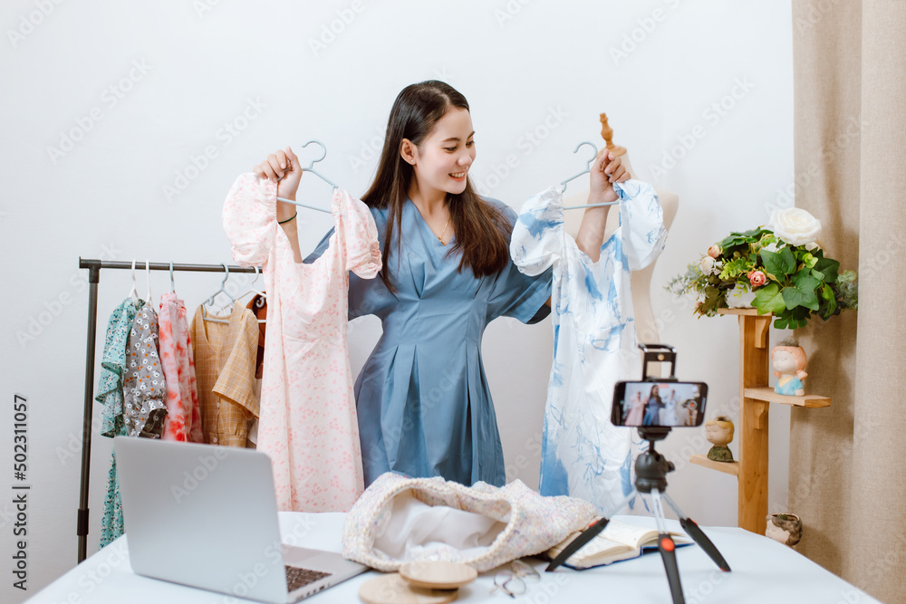 美丽的亚洲女人在她的店里用智能手机在线直播销售衣服。小生意