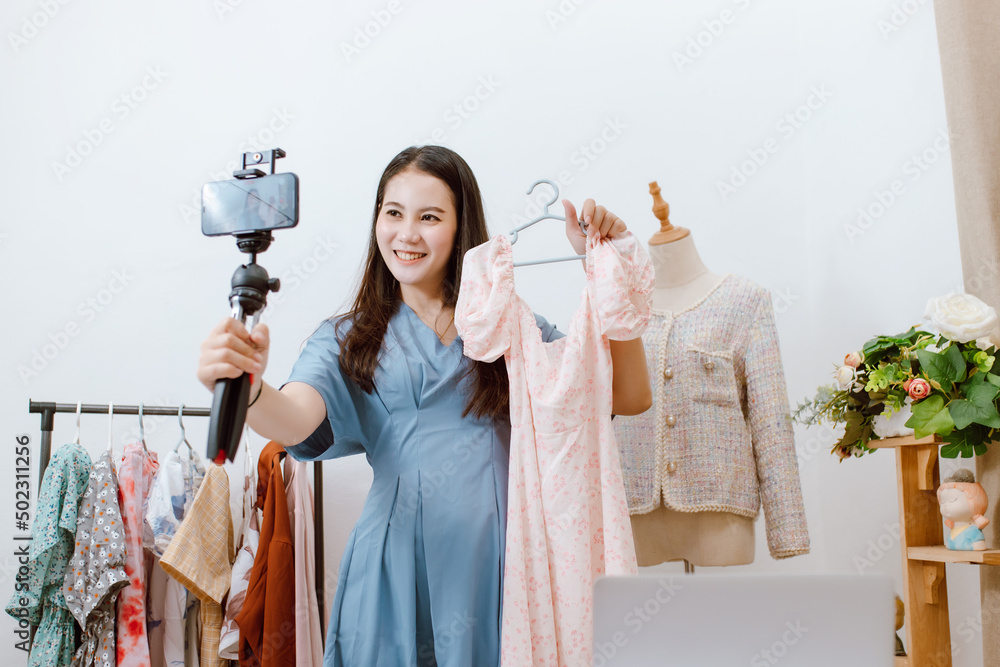 美丽的亚洲女人在她的店里用智能手机在线直播卖衣服。小生意