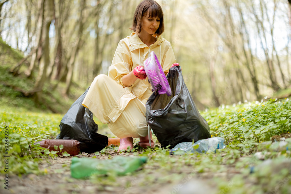 Young woman in protective clothes collecting scattered plastic garbage in the woods. Problem of bed 