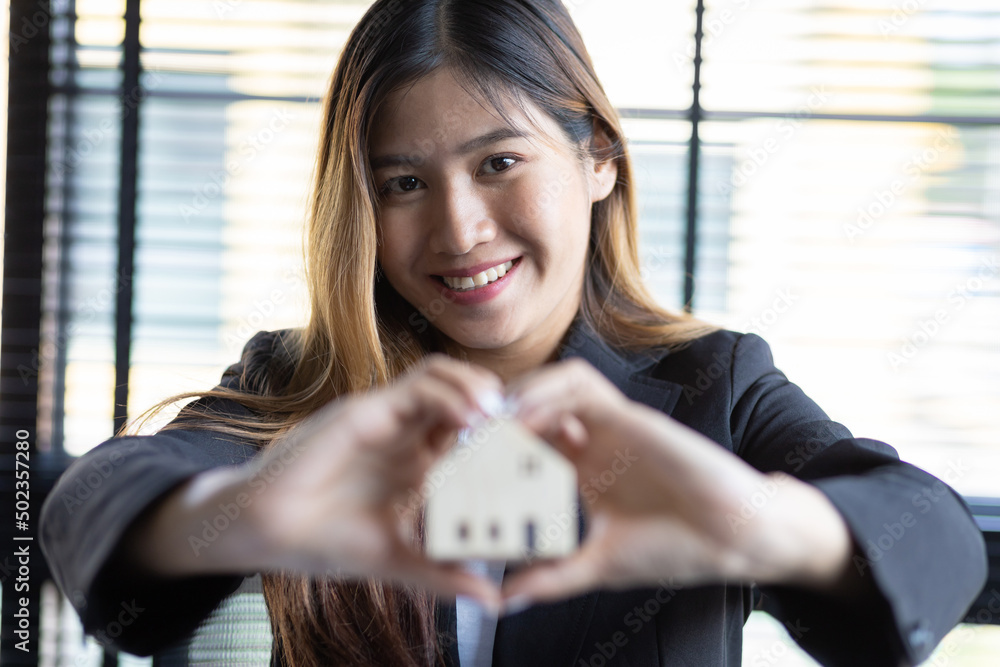 Businesswoman or insurance agent holding a house model. Real estate and home insurance concepts.