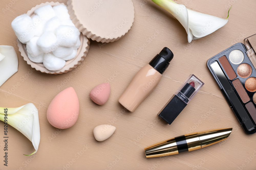 Composition with decorative cosmetics, makeup sponges, cotton balls and calla lilies on color wooden