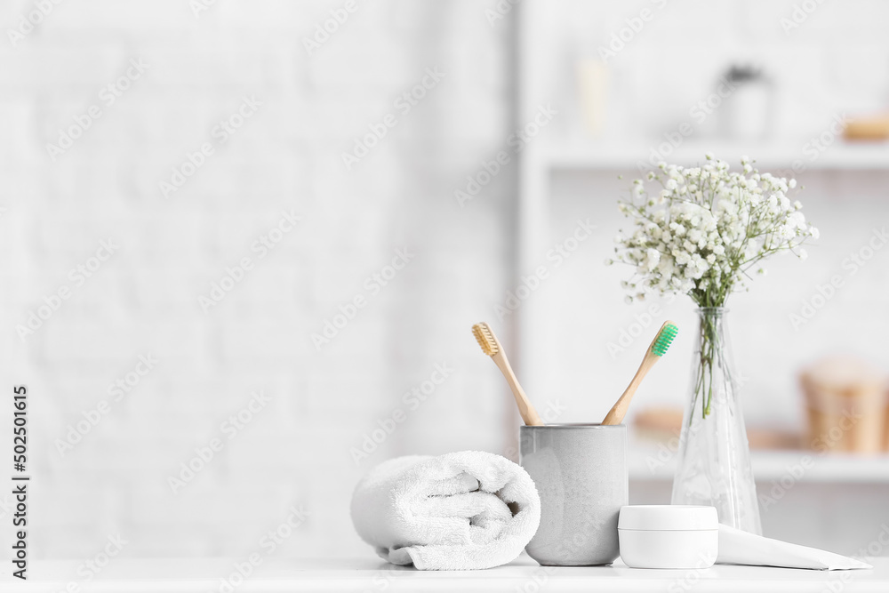 Holder with toothbrushes, jar of cream and rolled towel on table in bathroom