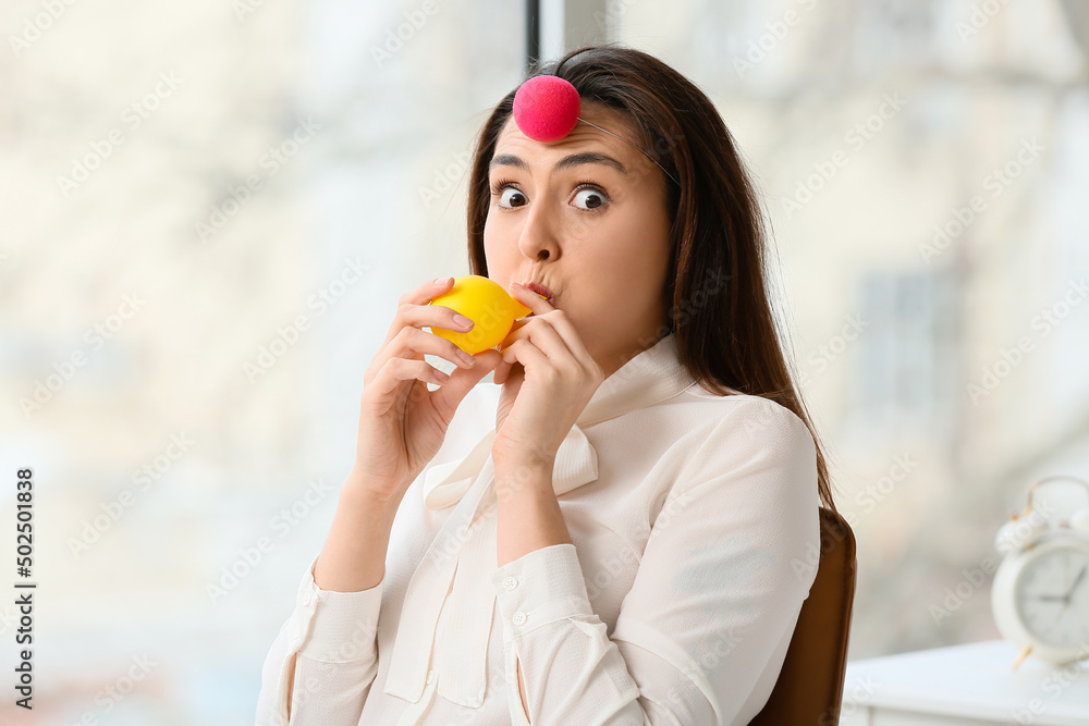 Funny young woman with clown nose and balloon in office. April fools day celebration