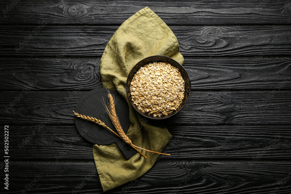 Bowl of raw oatmeal and spikelets on dark wooden background