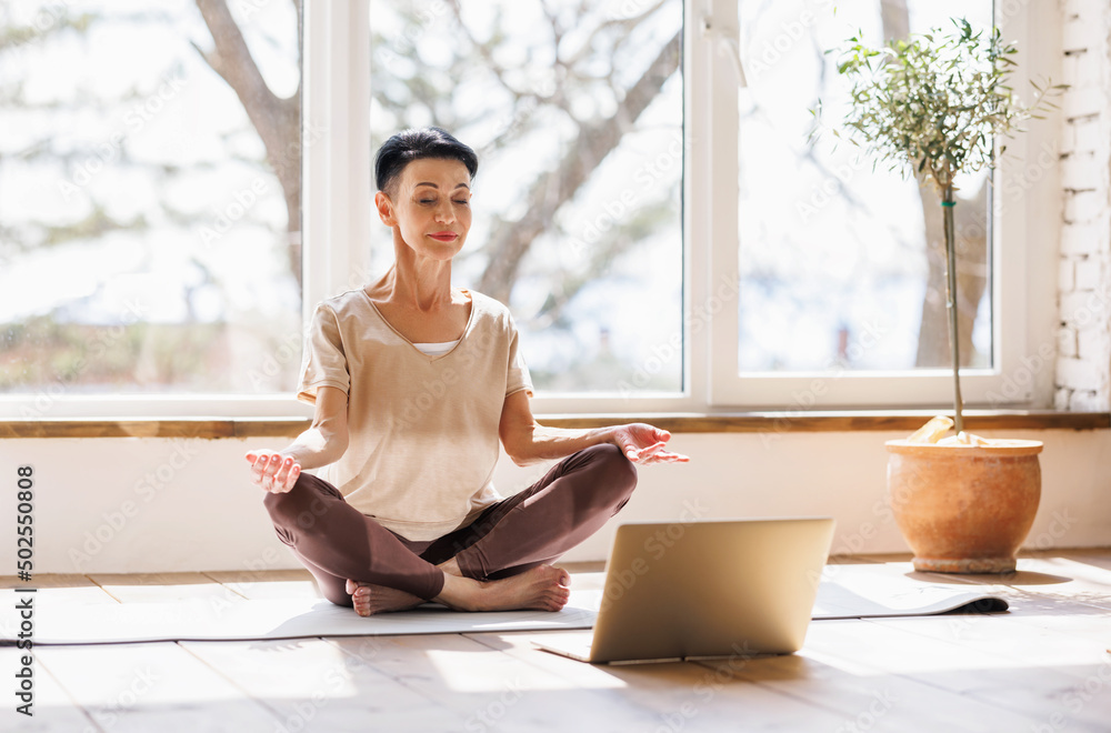 Mature woman meditating near laptop