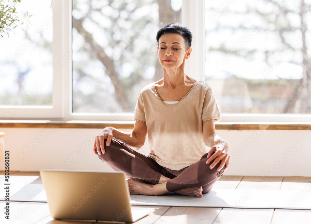 Mature woman meditating near laptop