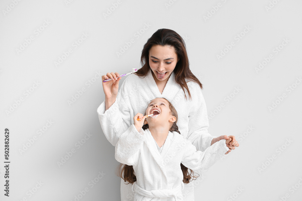 Little girl with her mother brushing teeth on light background