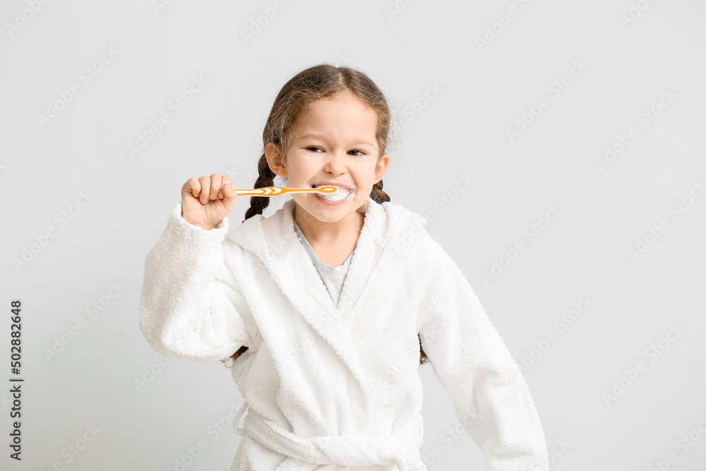 Adorable little girl brushing teeth on light background