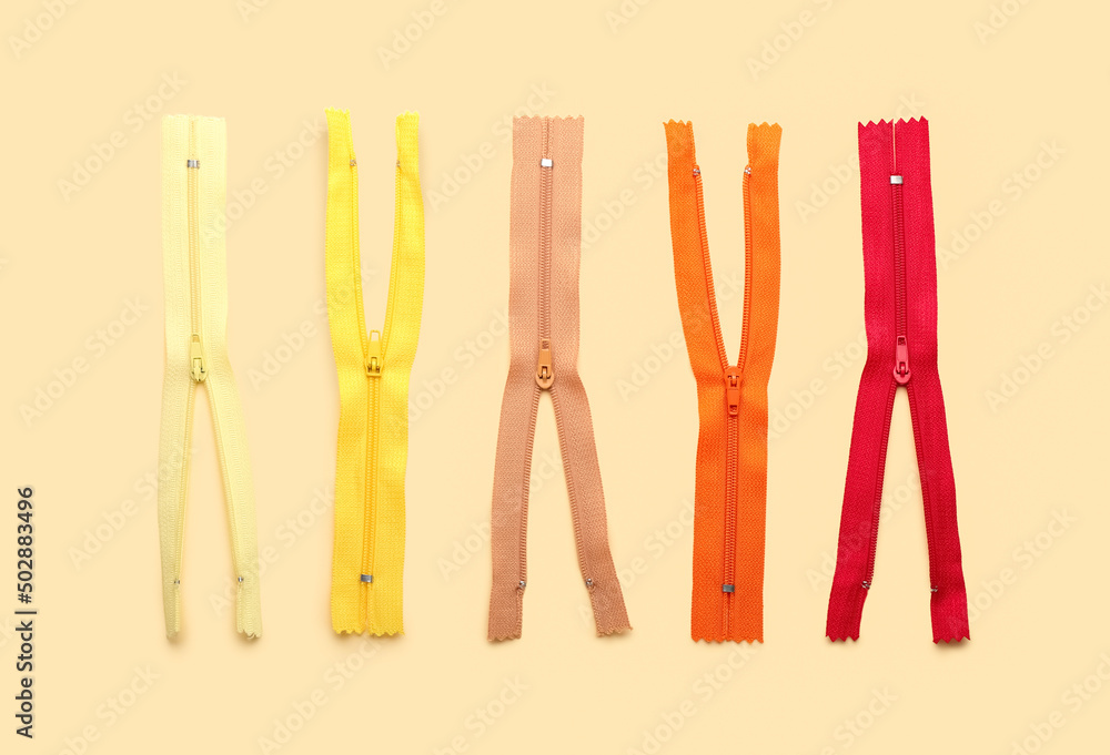 Stylish different zippers on beige background