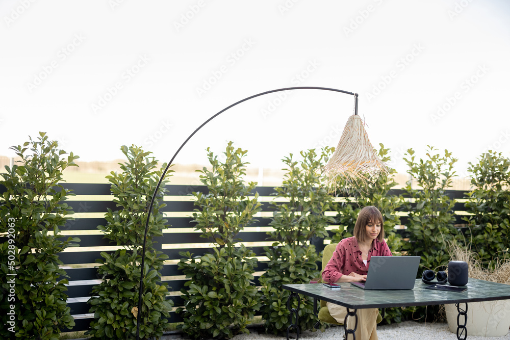 Young woman works on laptop at cozy outdoor workspace in the garden. Concept of remote work from com