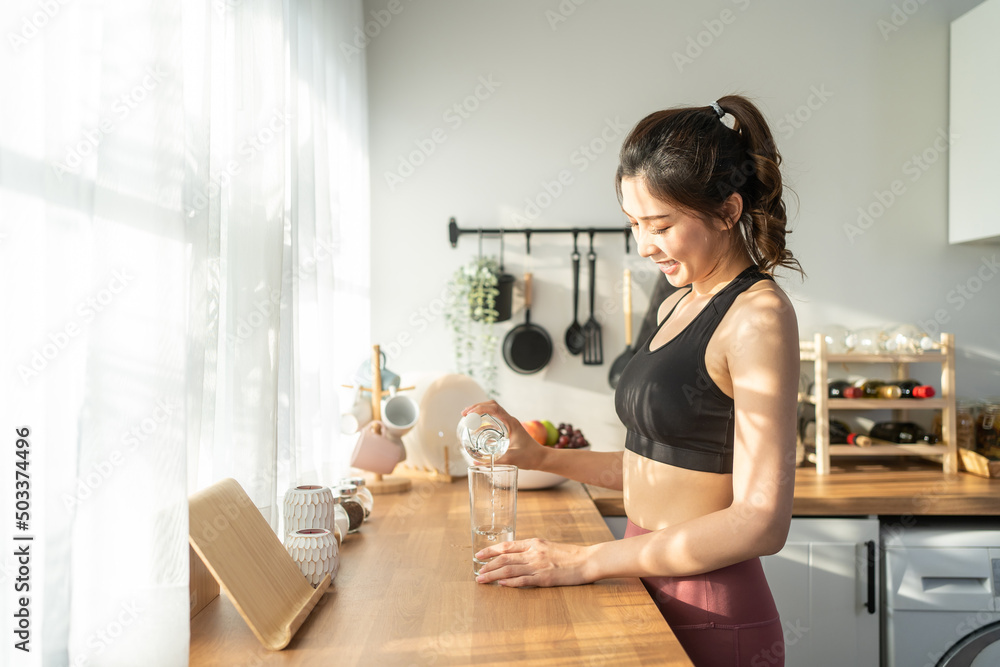 穿着运动服的亚洲美女在家锻炼后喝水。