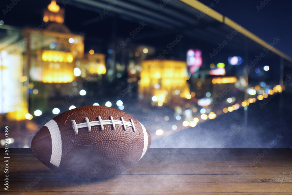 Rugby ball on wooden table against blurred night city