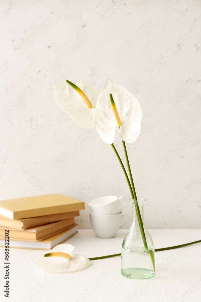 Vase with beautiful anthurium flowers, books and cups on light table