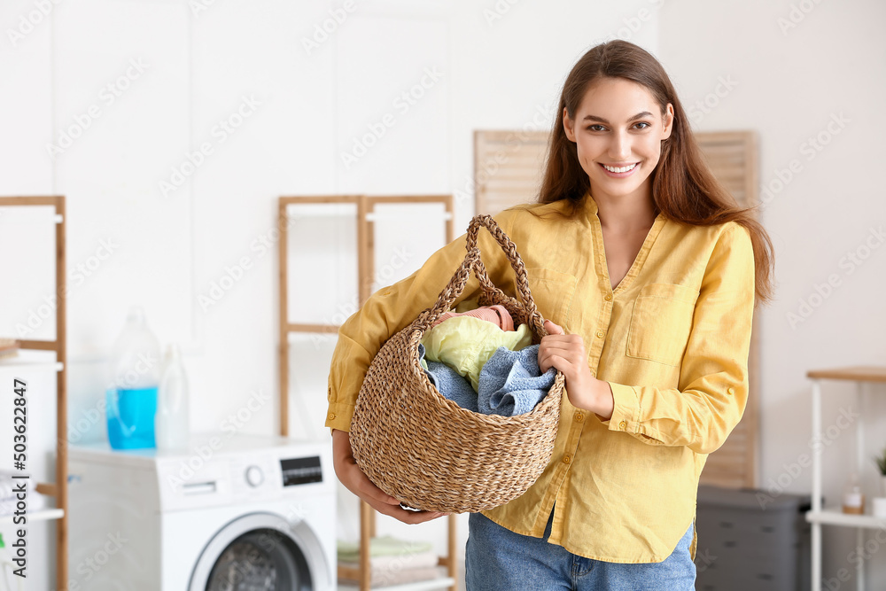 Beautiful housewife holding wicker basket with laundry at home