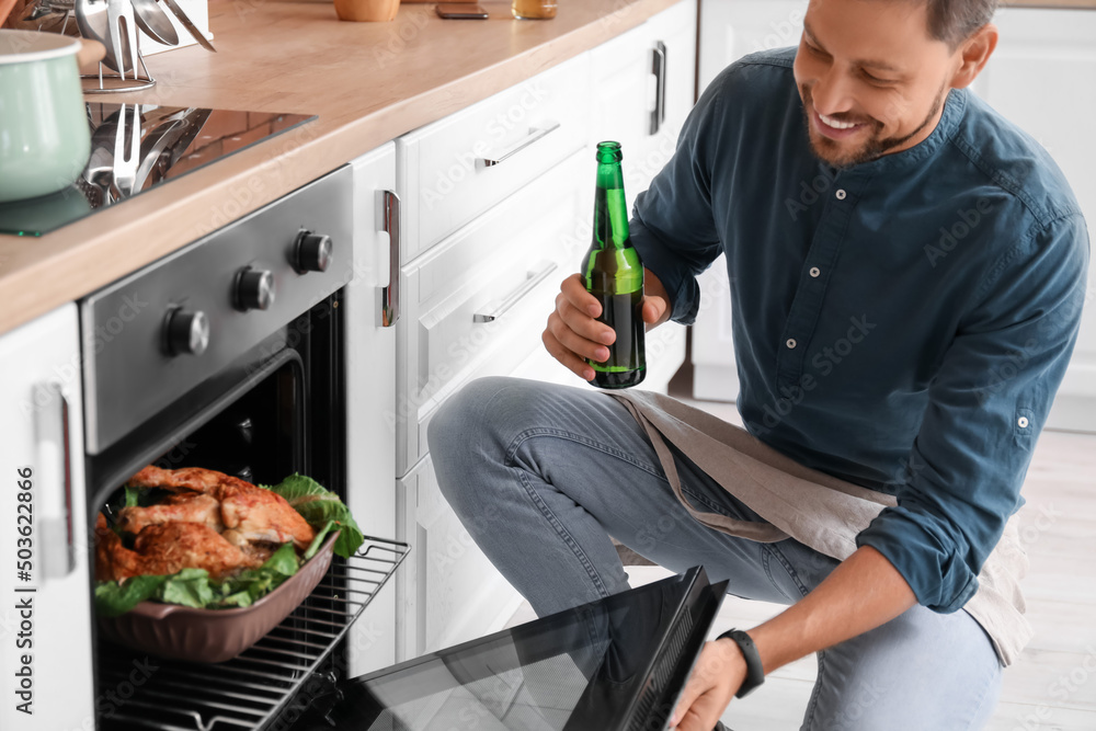 Handsome man drinking beer while cooking in kitchen