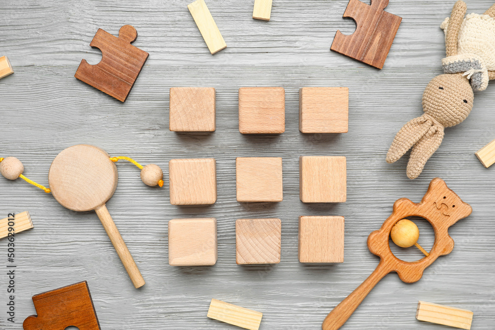 Cubes with baby toys on grey wooden background