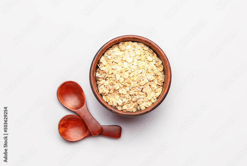 Bowl of raw oatmeal and spoons on white background