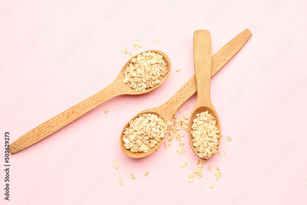 Wooden spoons with raw oatmeal on pink background