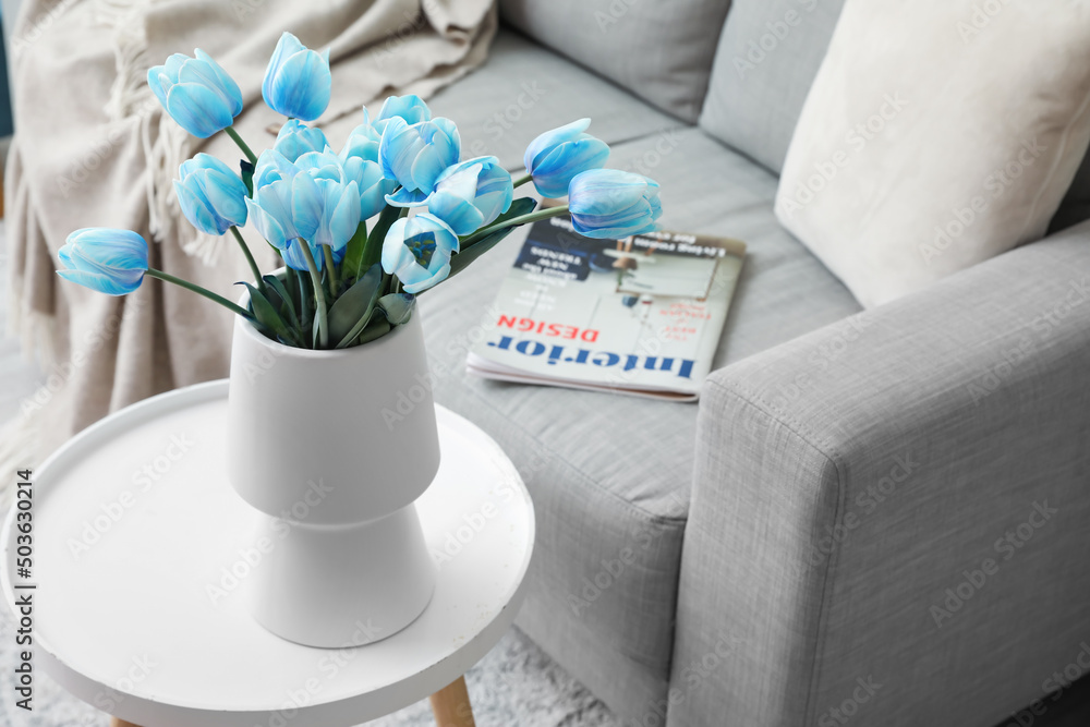 Vase with blue tulips on table in light living room