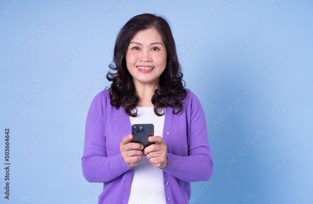 Portrait of middle aged Asian woman using smartphone on blue background