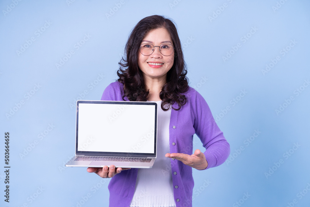 Portrait of middle aged Asian woman using laptop on blue background