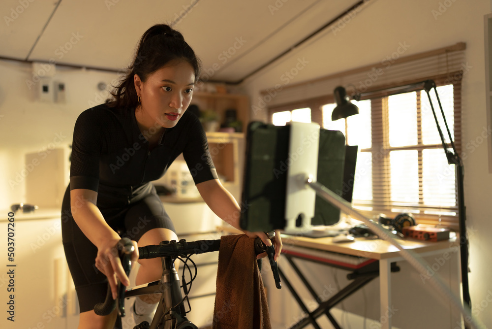 Female Asian cyclist, She is exercising at home. She rides a bike simulator.