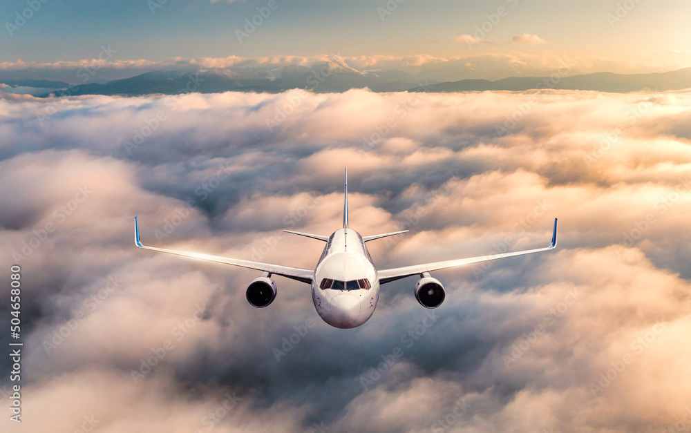 Airplane is flying above the clouds at sunrise in summer. Landscape with passenger airplane, beautif