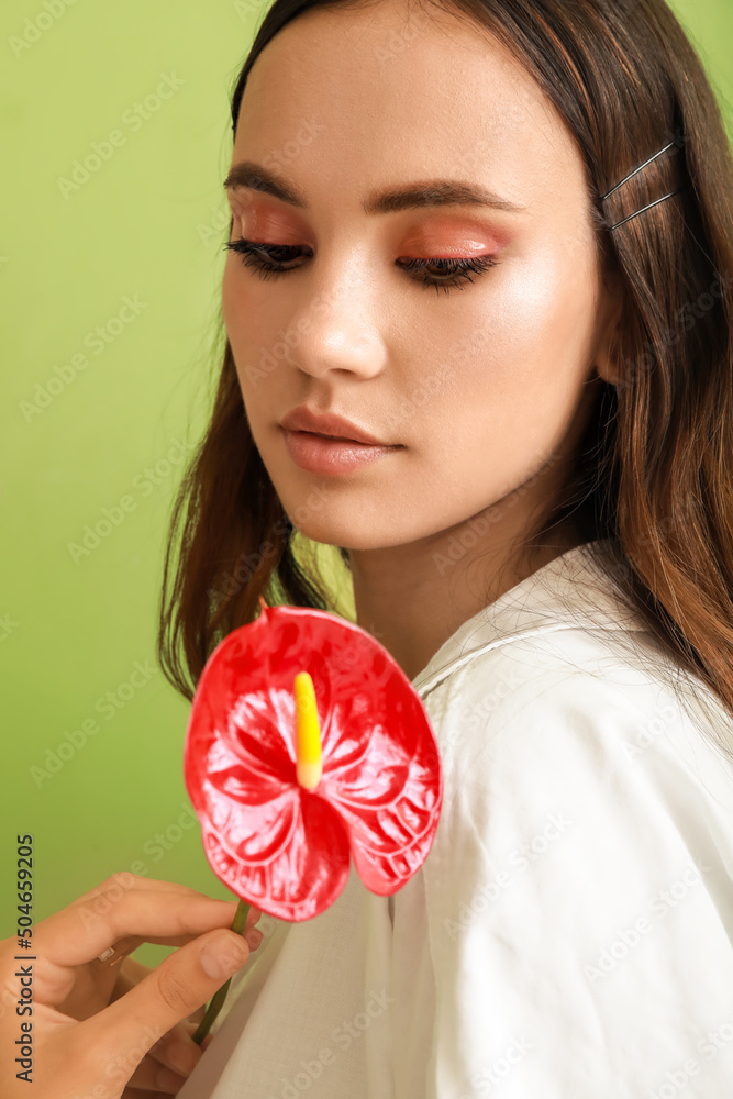 Beautiful young woman looking at anthurium flower in her hand on green background