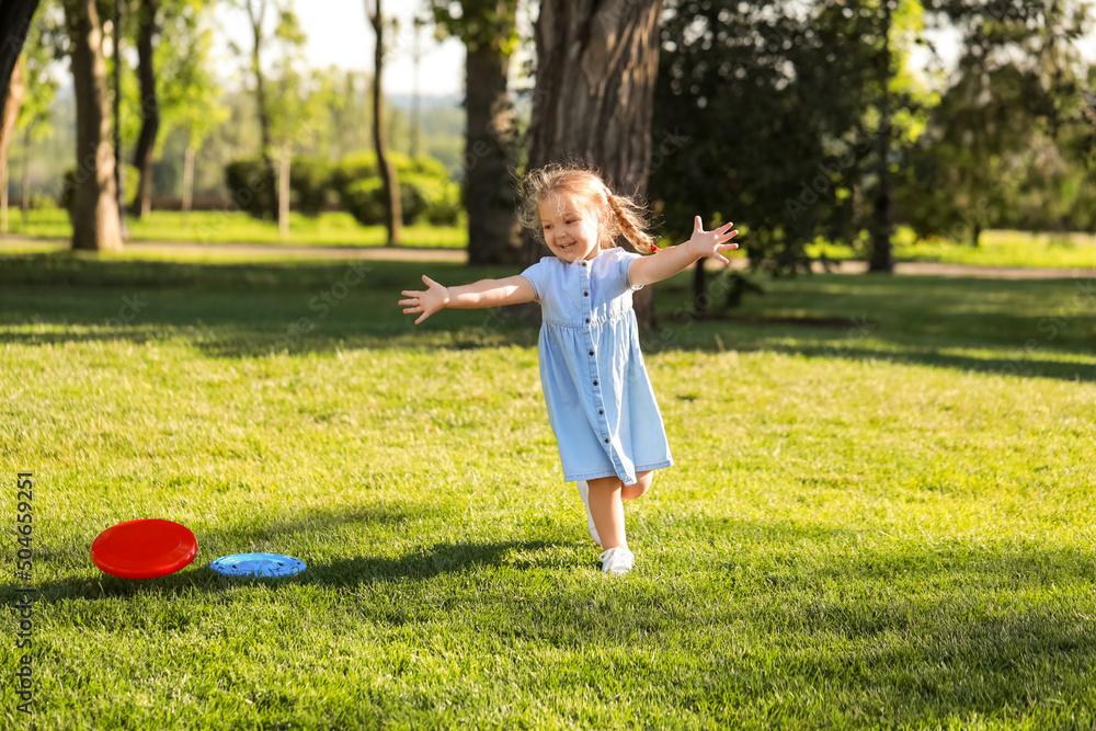 Cute little girl in blue dress playing frisbee in park