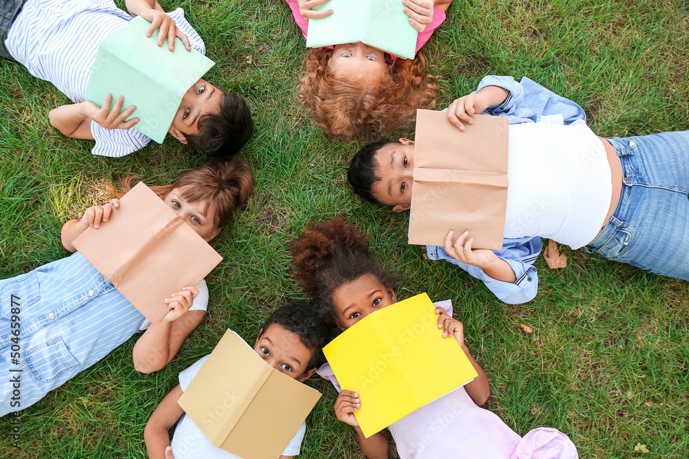 Little children with books lying on green grass in park