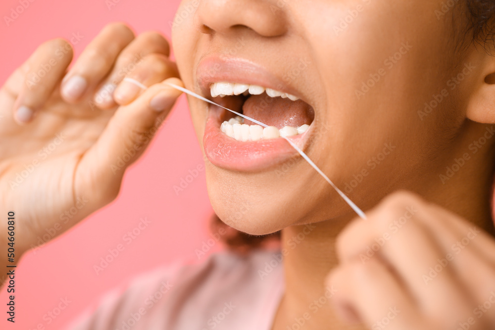 African-American teenage girl flossing teeth on pink background, closeup