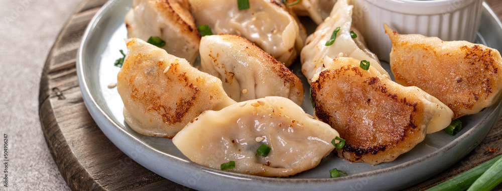 灰色桌子背景上放着酱油的盘子里的煎饺子饺子饺子。