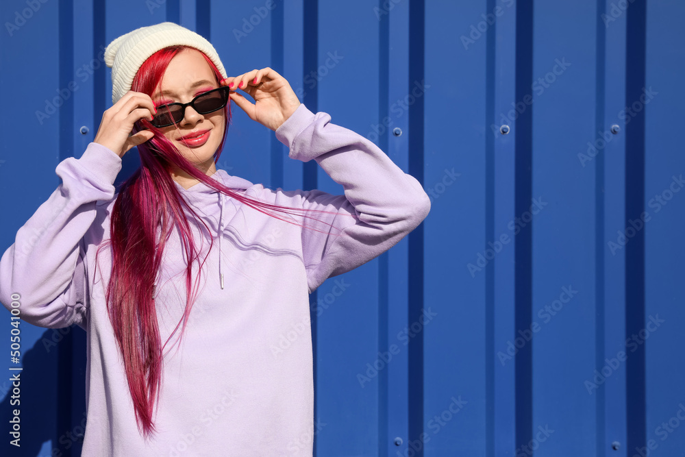 Beautiful woman with bright hair in sunglasses on blue background