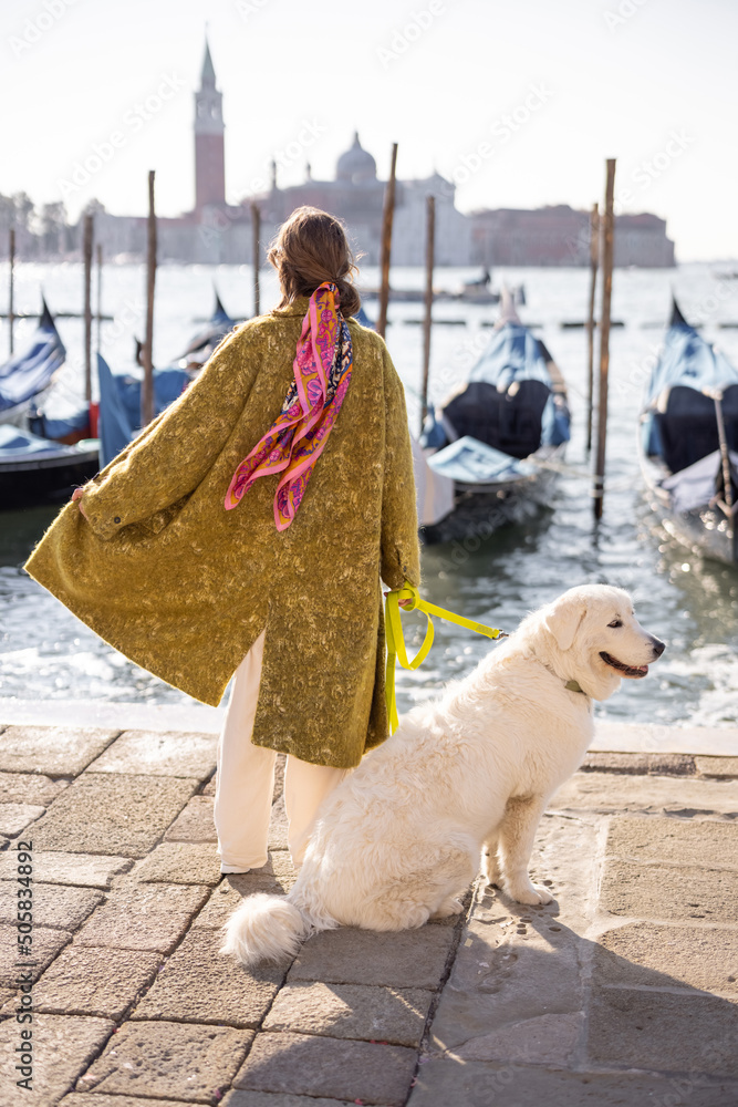 Young woman walking with dog near water canal with gondolas at saint Marks square in Venice. Woman w