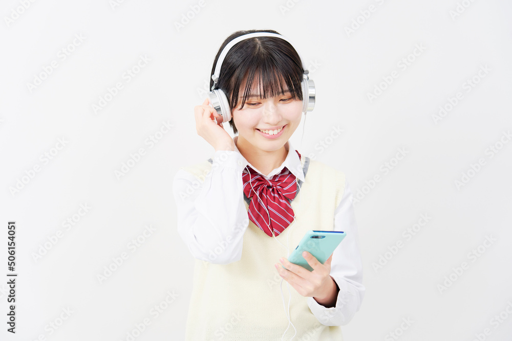 白背景でヘッドホンでスマホを使って音楽を聴く女子高生