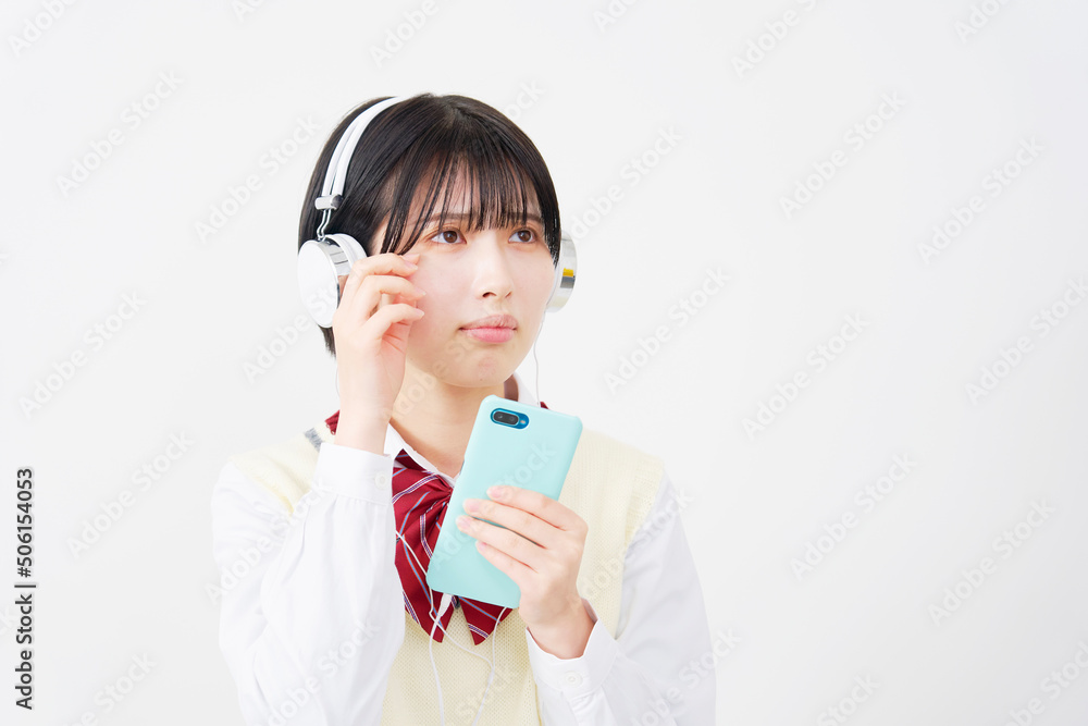 白背景でヘッドホンでスマホを使って泣きながら音楽を聴く女子高生