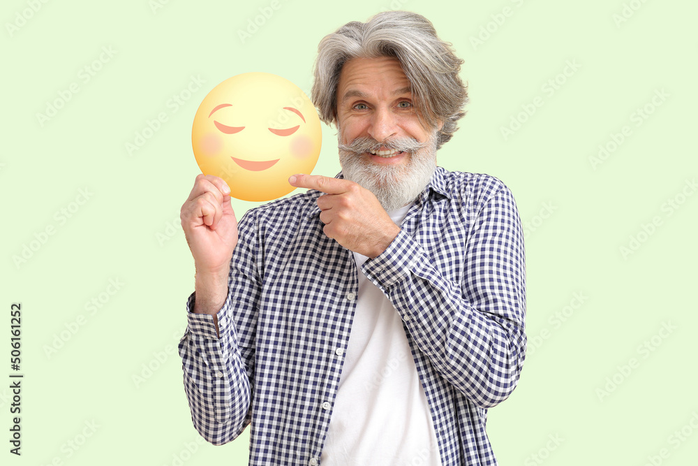 Happy senior man holding smiling emoticon on light color background