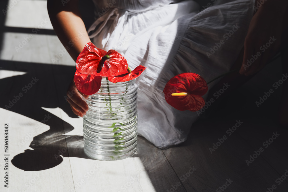 Woman sitting on floor and holding vase with beautiful anthurium flowers