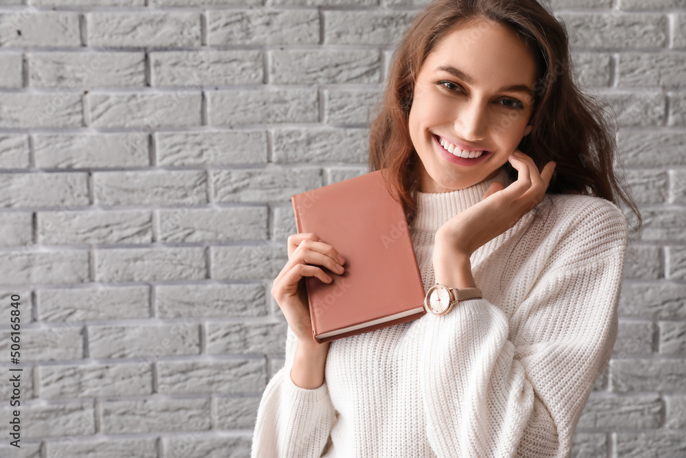 Pretty smiling woman with book near grey brick wall