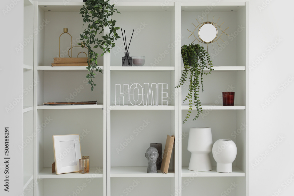 Shelving unit with vases, houseplants and decor near light wall