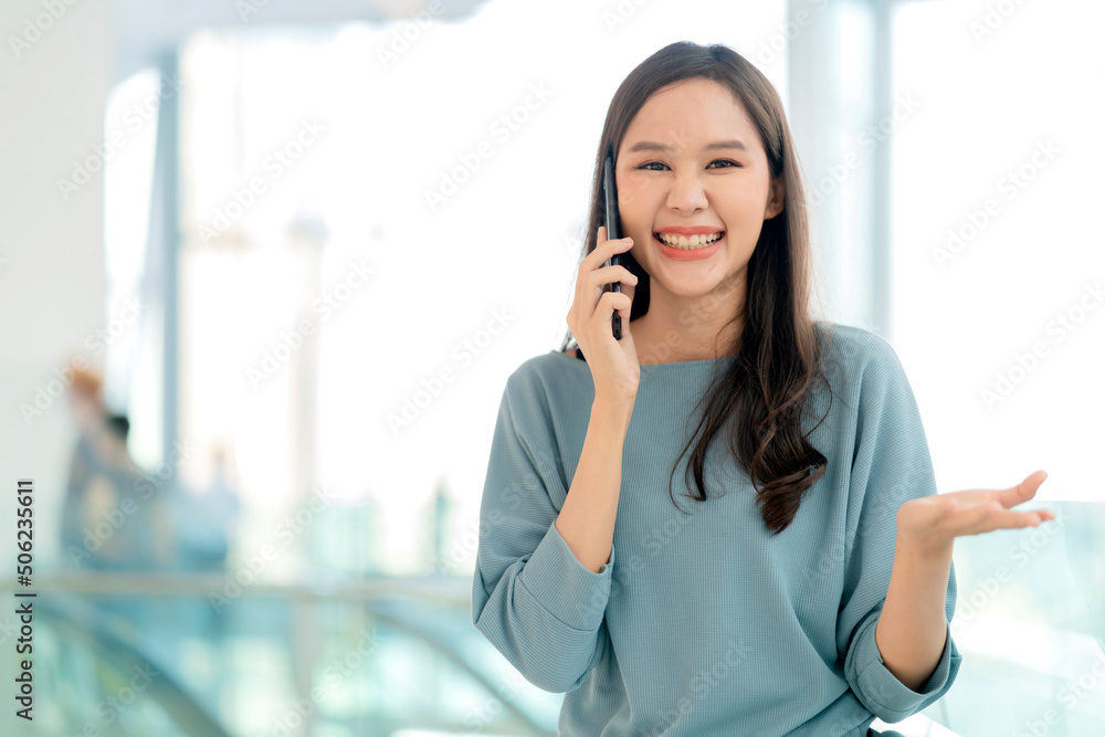 微笑的亚洲女青少年在购物中心与密友用智能手机交谈