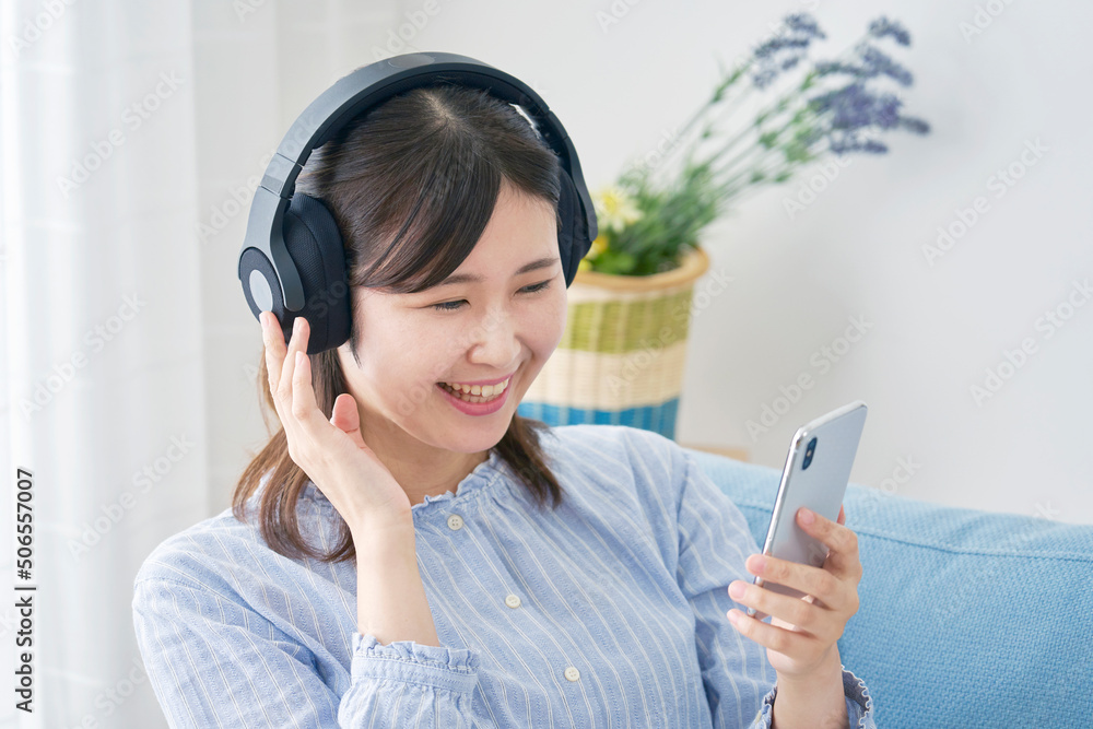 リビングでヘッドホンをしてスマホで音楽を聴く女性