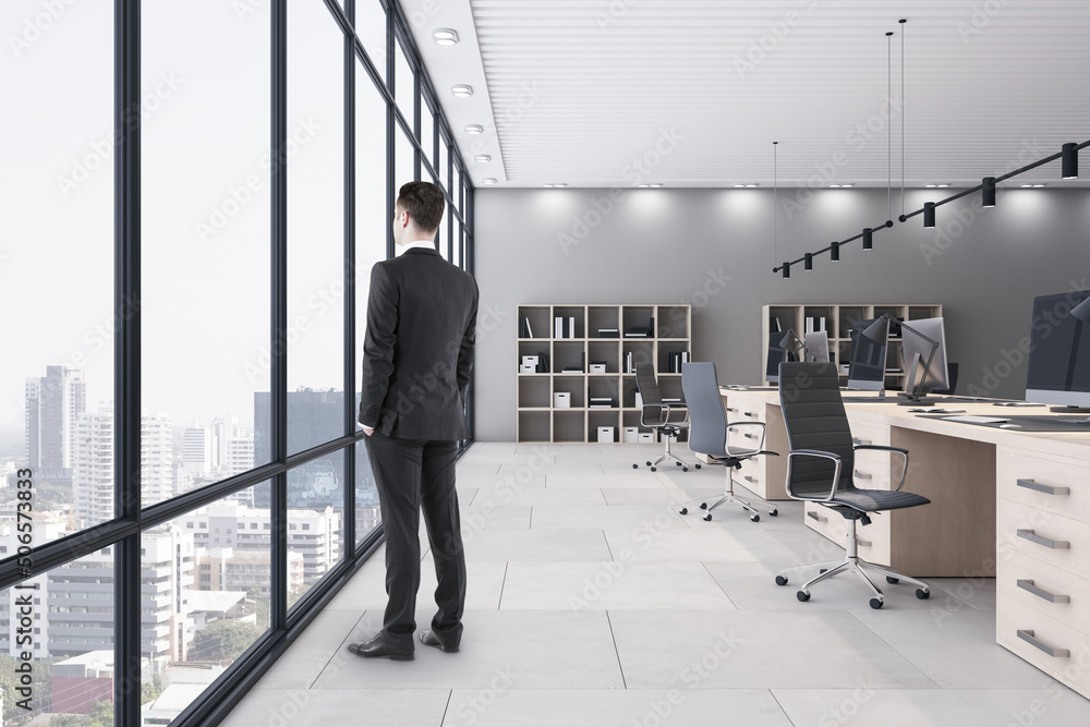 Business success concept with back view on businessman looking through huge window on city skyscrape