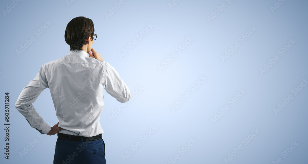 Thinking concept with pensive man in white shirt standing on abstract light blue wall backdrop, with