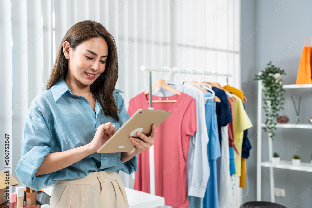 Asian young woman standing use tablets sell clothing online in office.