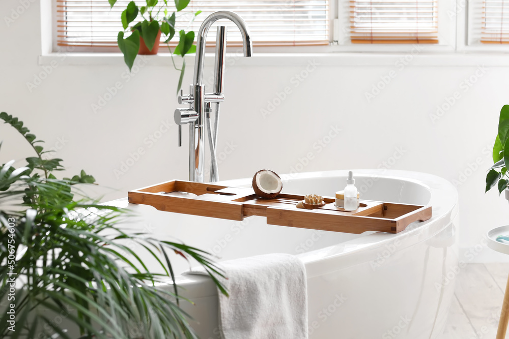 Tray with coconut oil and massage brush on bathtub in light room