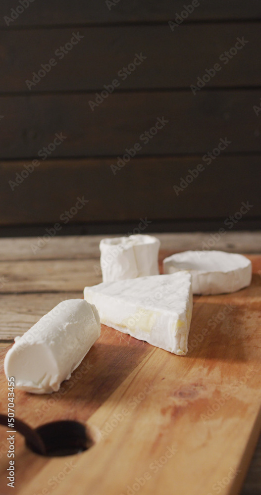 Vertical image of few types of fresh cheese on wooden chopping board and rustic background